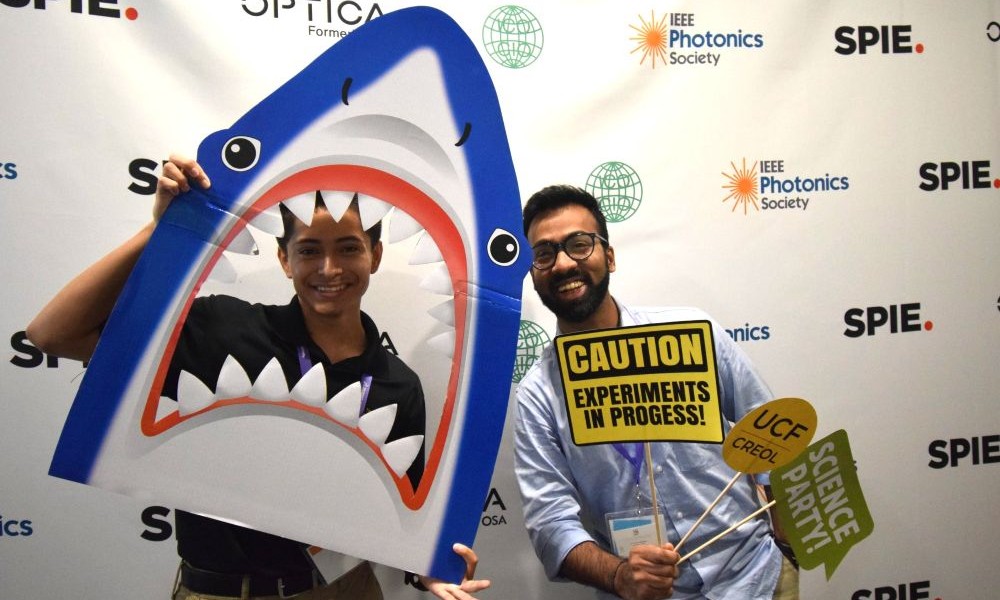 ETOP conference attendees pose with a shark cut-out and "Caution: Experiments in Progress!" sign in a photo booth