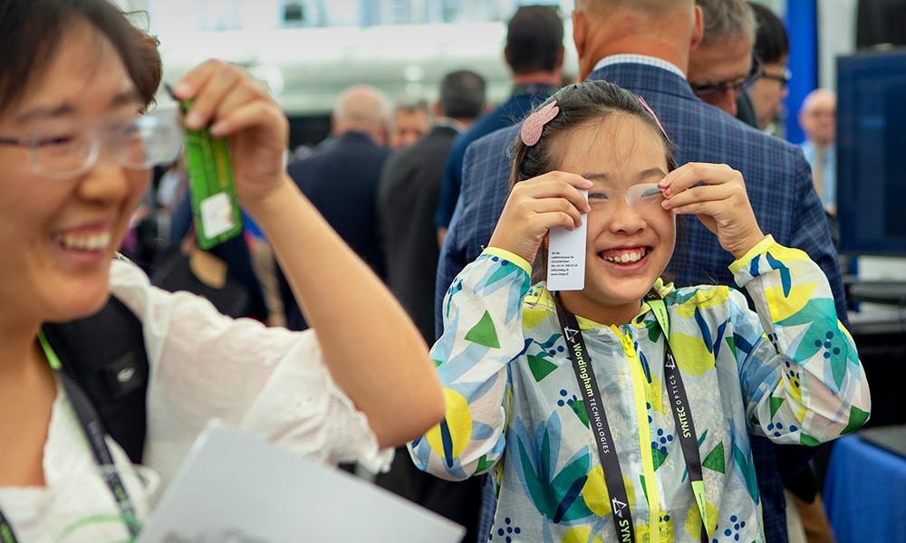 A woman and a girl smile happily as they put lenses on their eyes at an outreach event