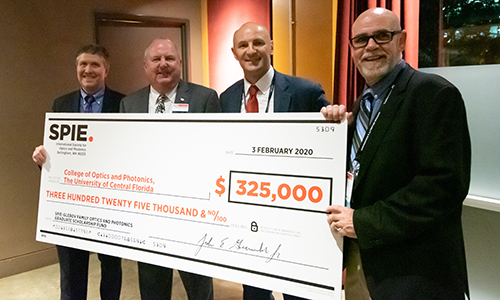 Four people holding up an oversized check for $325,000, made out to the University of Central Florida, College of Optics and Photonics