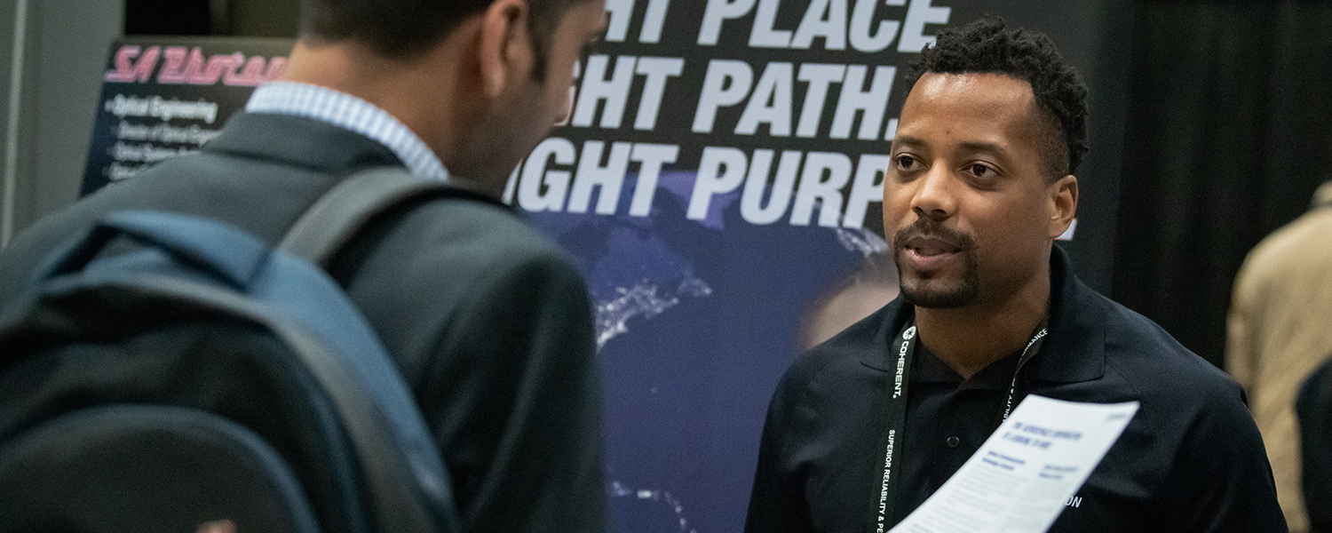 An exhibitor speaks with an interested attendee in his booth