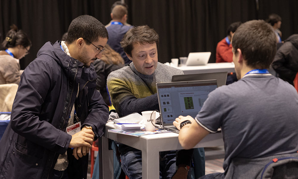 Two males collaborate at a laptop in room with other course takers