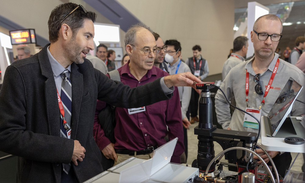 Three people gather around at an exciting laser exhibit at SPIE Photonics West