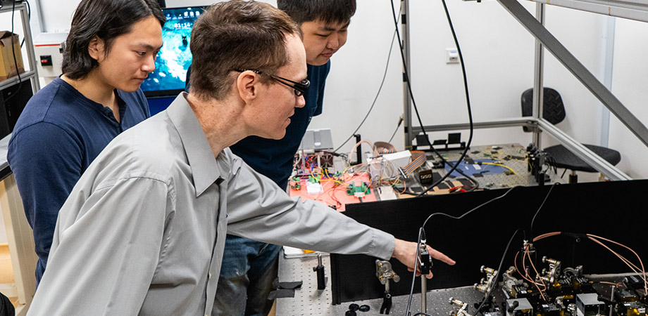 Associate Professor Aaron Danner, center, with PhD students Zifeng Yuan, left, and Yuan Gao, right, all from the NUS Department of Electrical and Computer Engineering, at an all-optical Ising machine that was designed and built by Gao. 